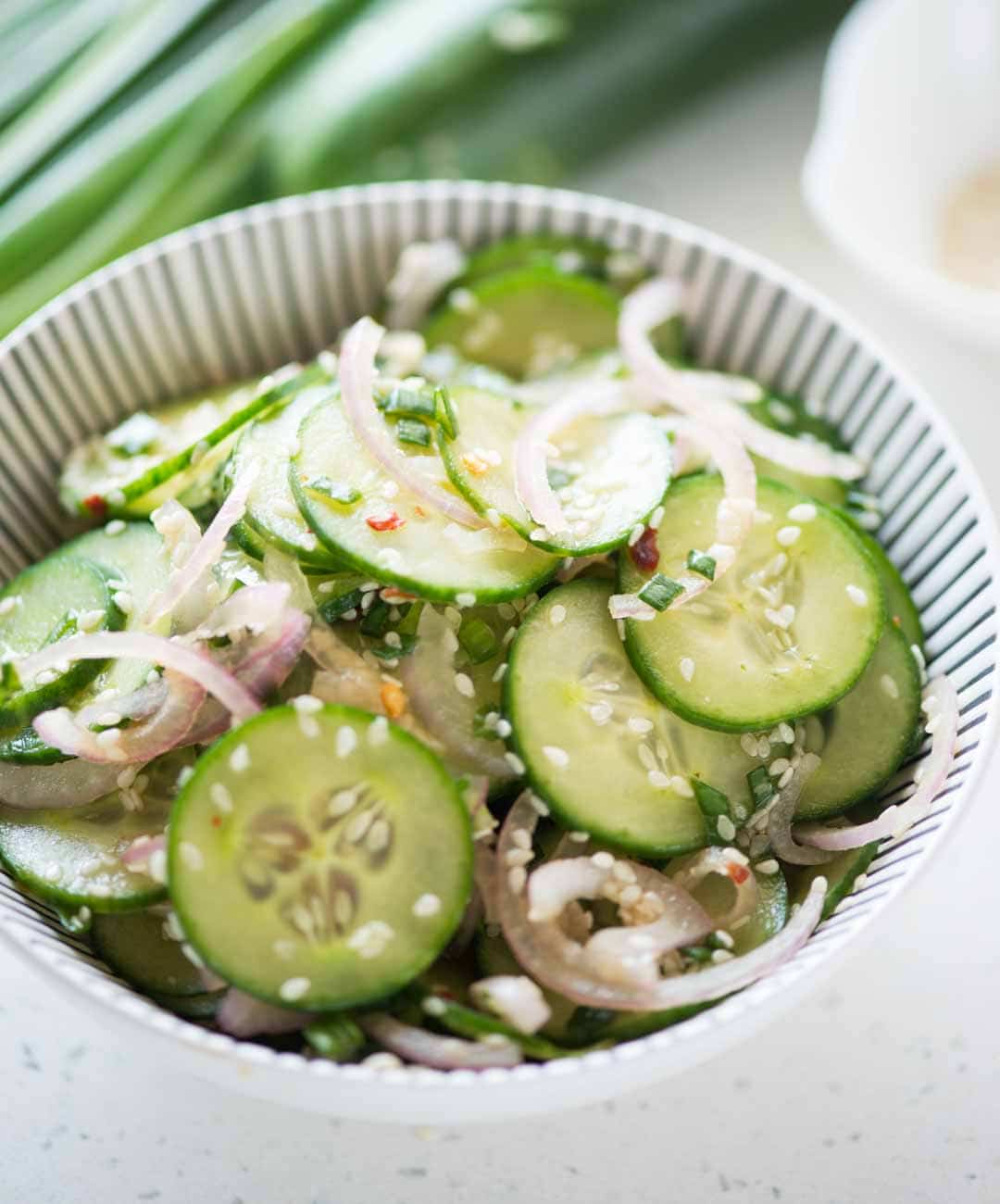 Cucumber salad with Asian salad dressing served in a white bowl.
