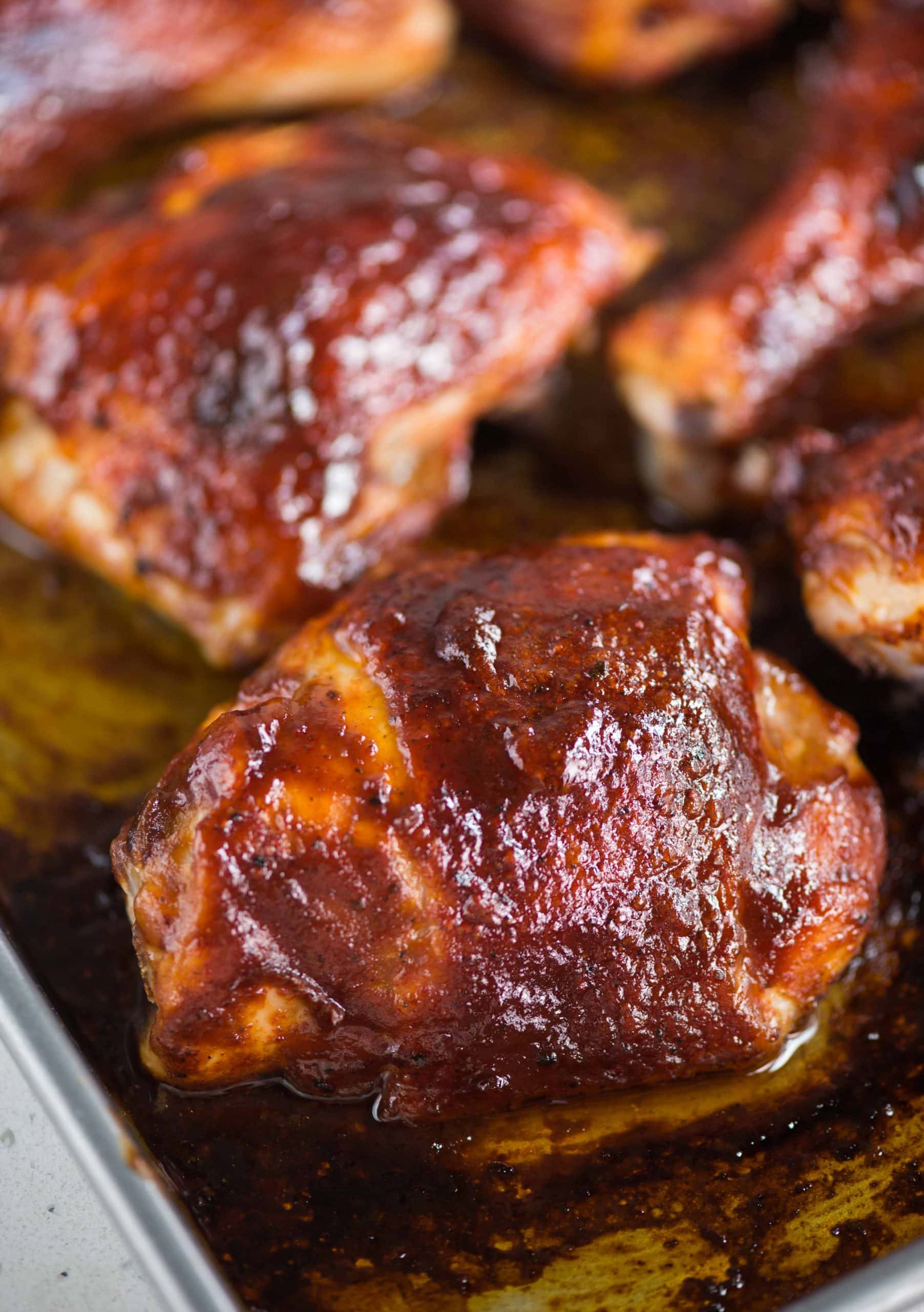 Close up view of baked chicken on a baking tray, with a BBQ sauce that has a crisp and charred skin.