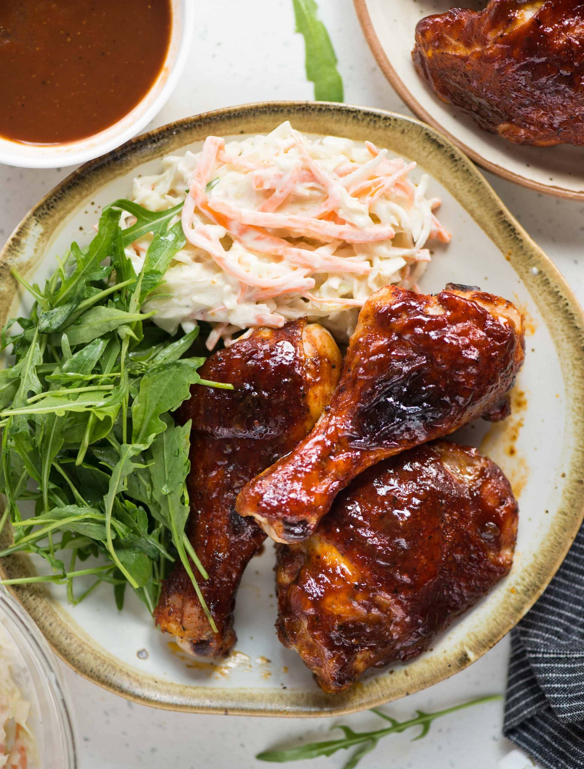 Oven baked BBQ chicken served with coleslaw and greens in a white plate.