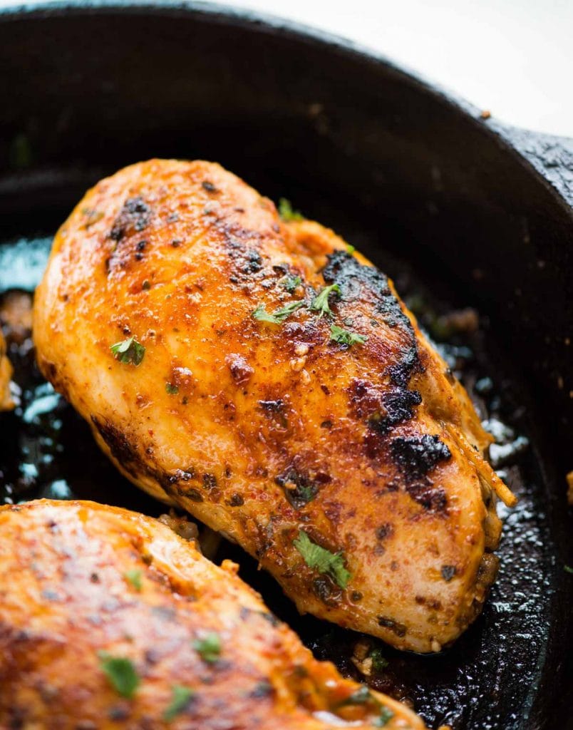 close up of stuffed chicken breast with mushroom and spinach stuffing inside it, cooked on a cast iron pan.