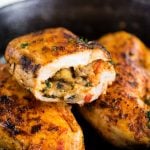Stuffed chicken breast is cut in half to show a oozing stuffing mixture of cheese, roasted mushroom, and spinach.