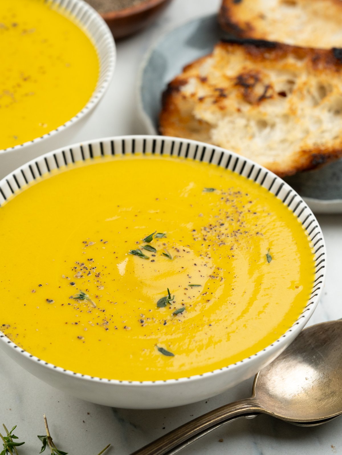 simple homemade pumpkin soup with freshly crushed black pepper and thyme served with crusty bread.