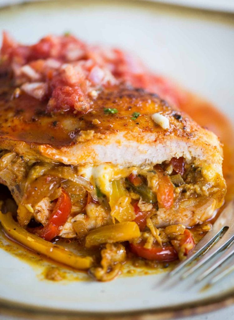 Close up image of stuffed and baked chicken breast shows fajita-stuffing consisting of onions, peppers, onion, and cheese.