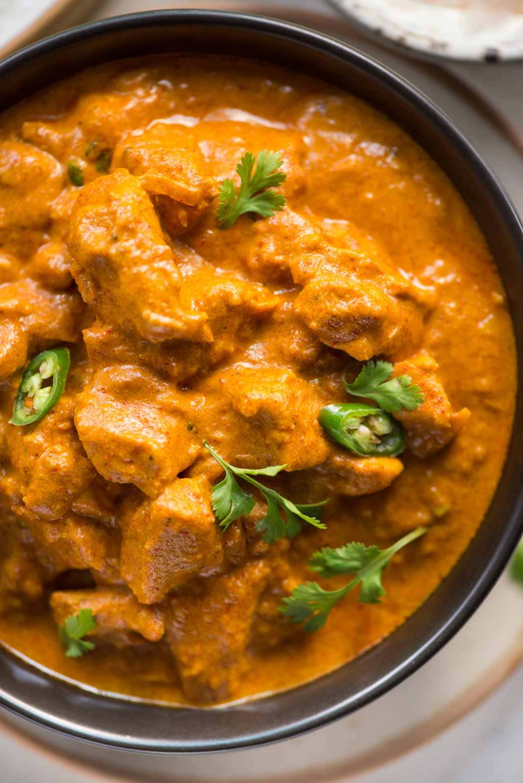 Chopped cilantro and green chilli garnished on top of creamy Coconut Chicken Curry and served in a black bowl.