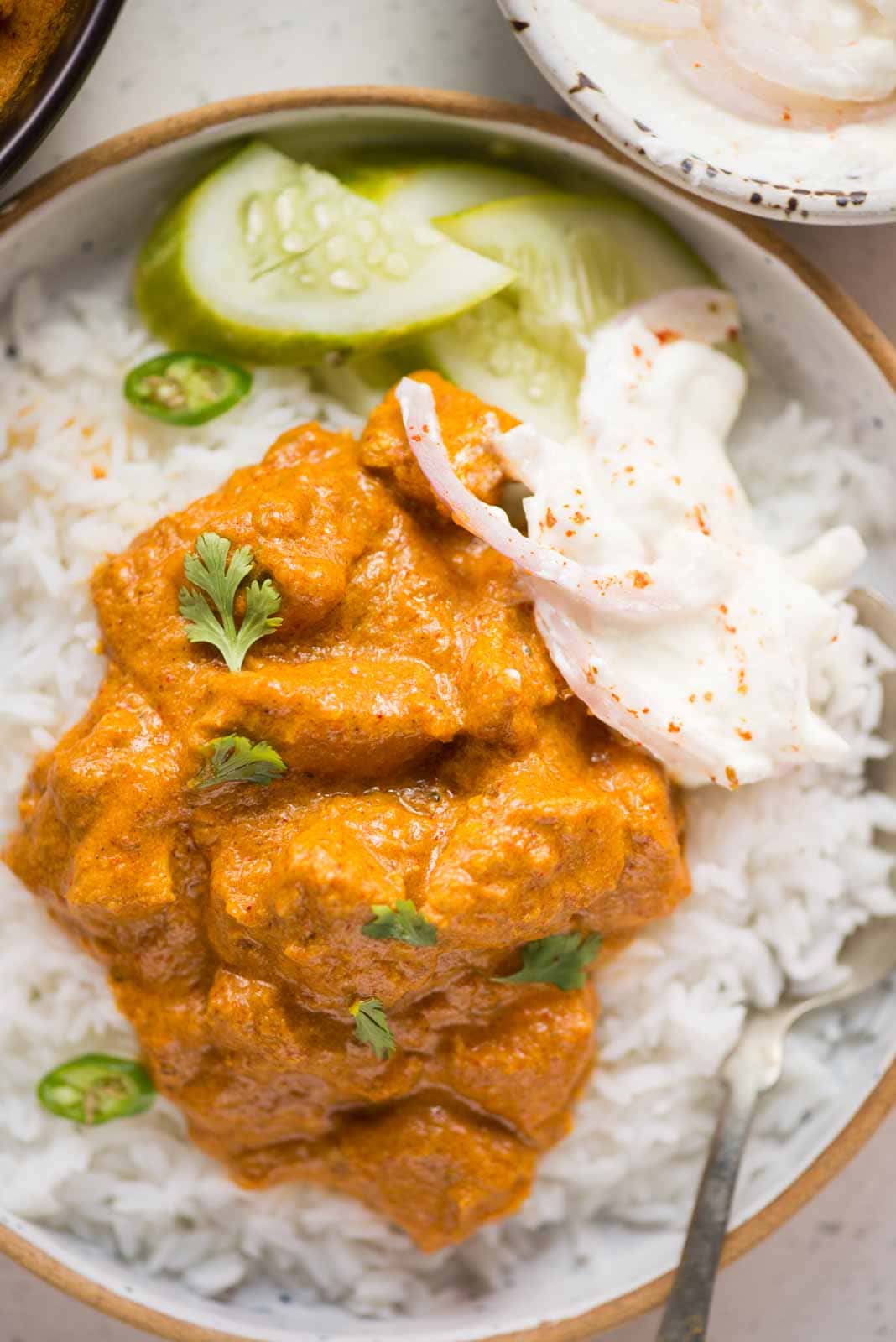 Creamy coconut chicken curry served on a bowl of white rice with chopped cucumber, sliced onion and chopped cilantro as garnish.