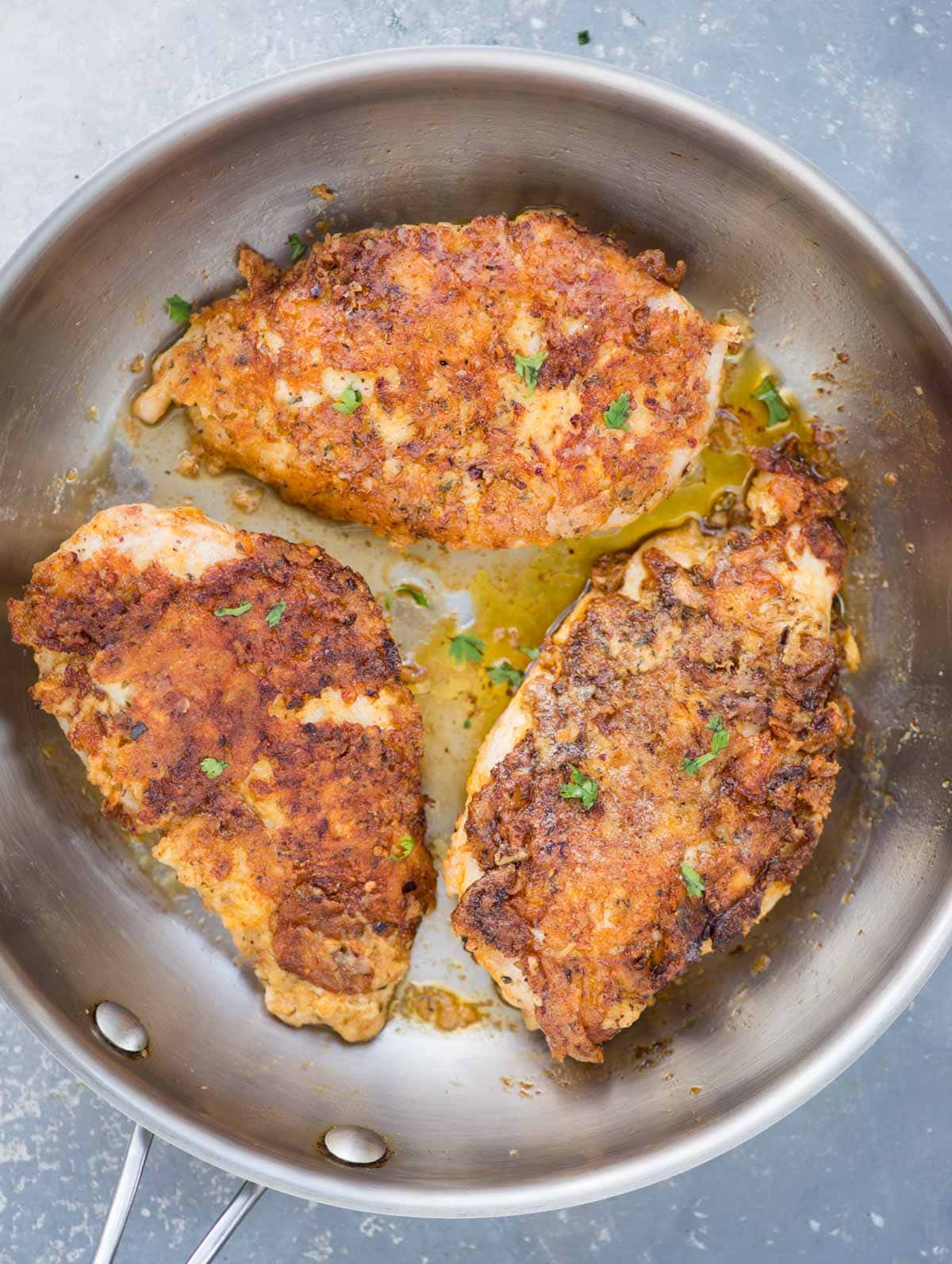 Three chicken breasts which are perfectly crispy on the crust and juicy underneath are fried on a pan.