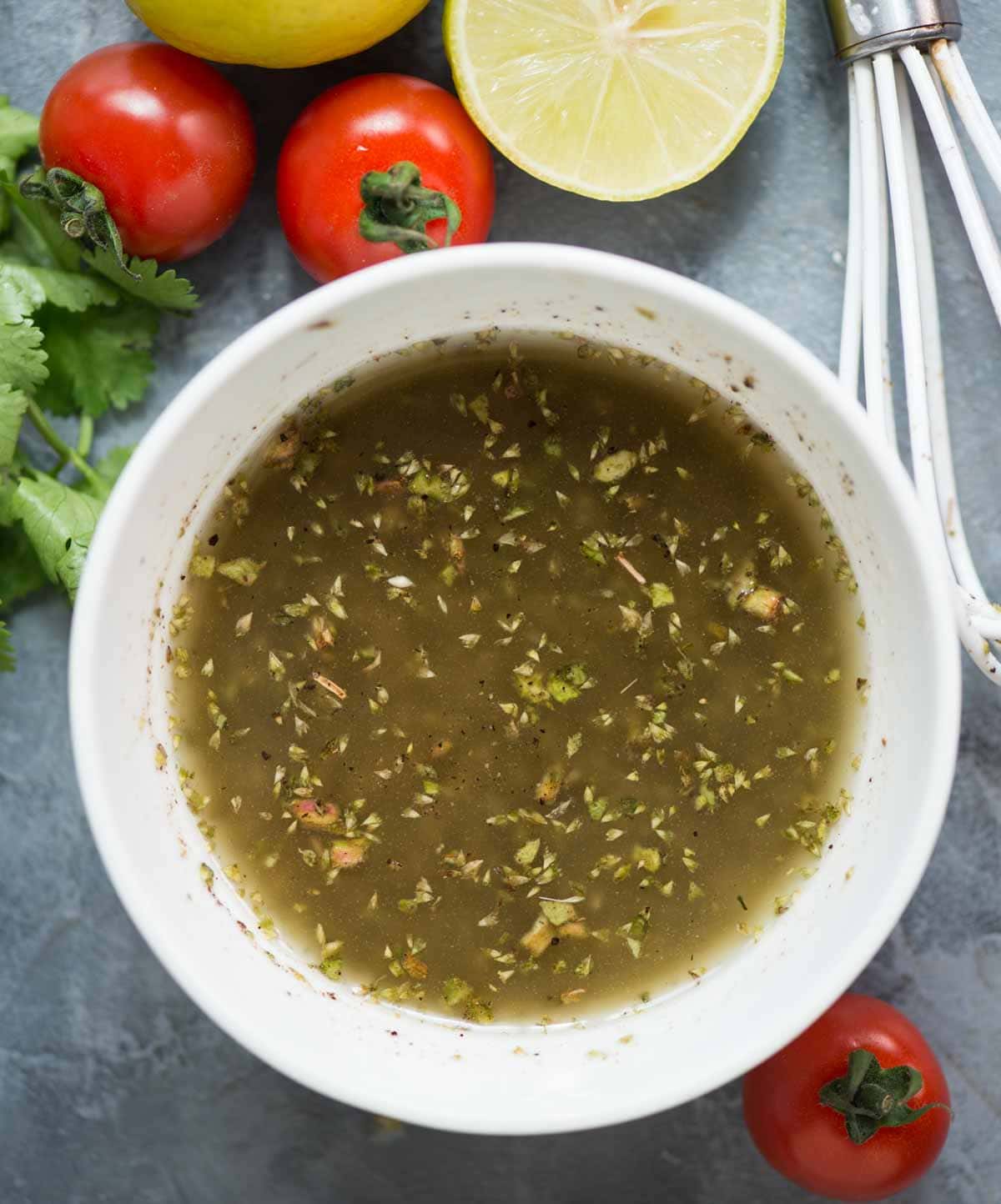 Lemon-Herb vinaigrette in a white bowl shown with cherry tomato, cilantro and lemon slices.