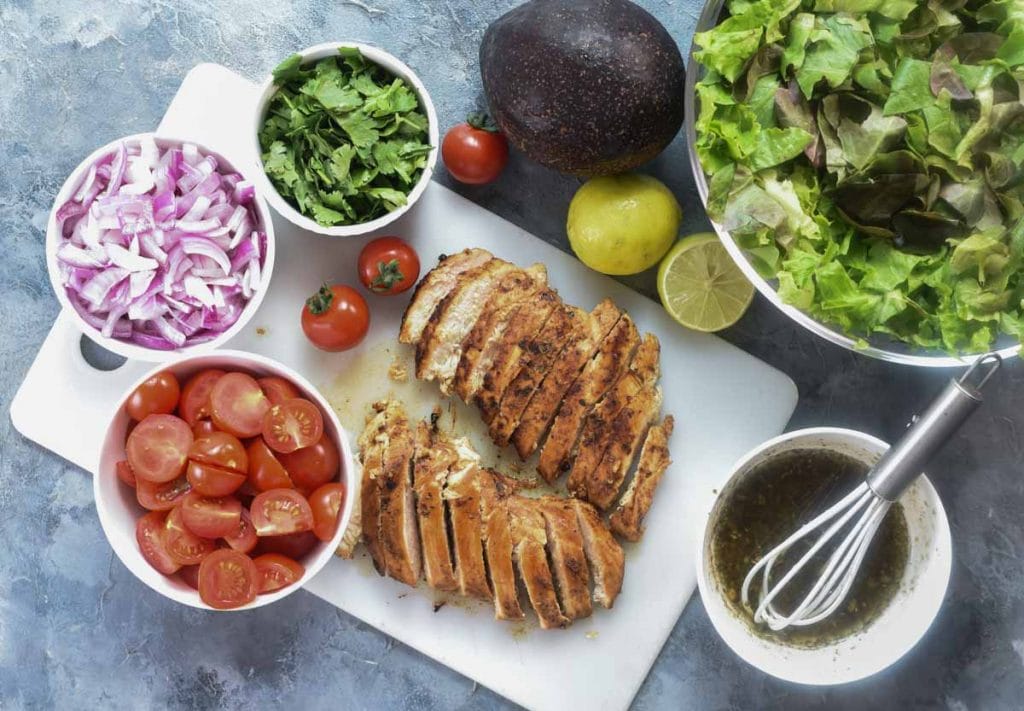 Showing all the ingredients needed for Chicken Salad with avocado shown in bowls and a board.