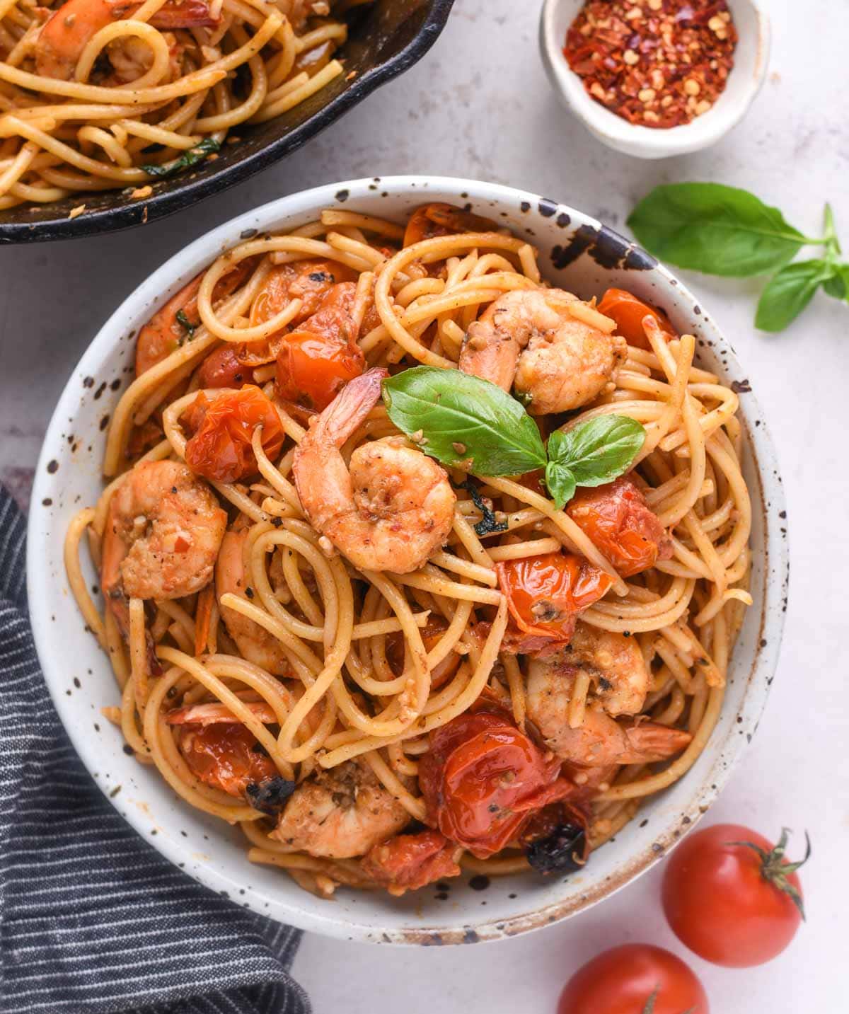 Cherry tomato pasta served in a white bowl. Cooked shrimps and cherry tomato sauce and fresh basil leaves on top.