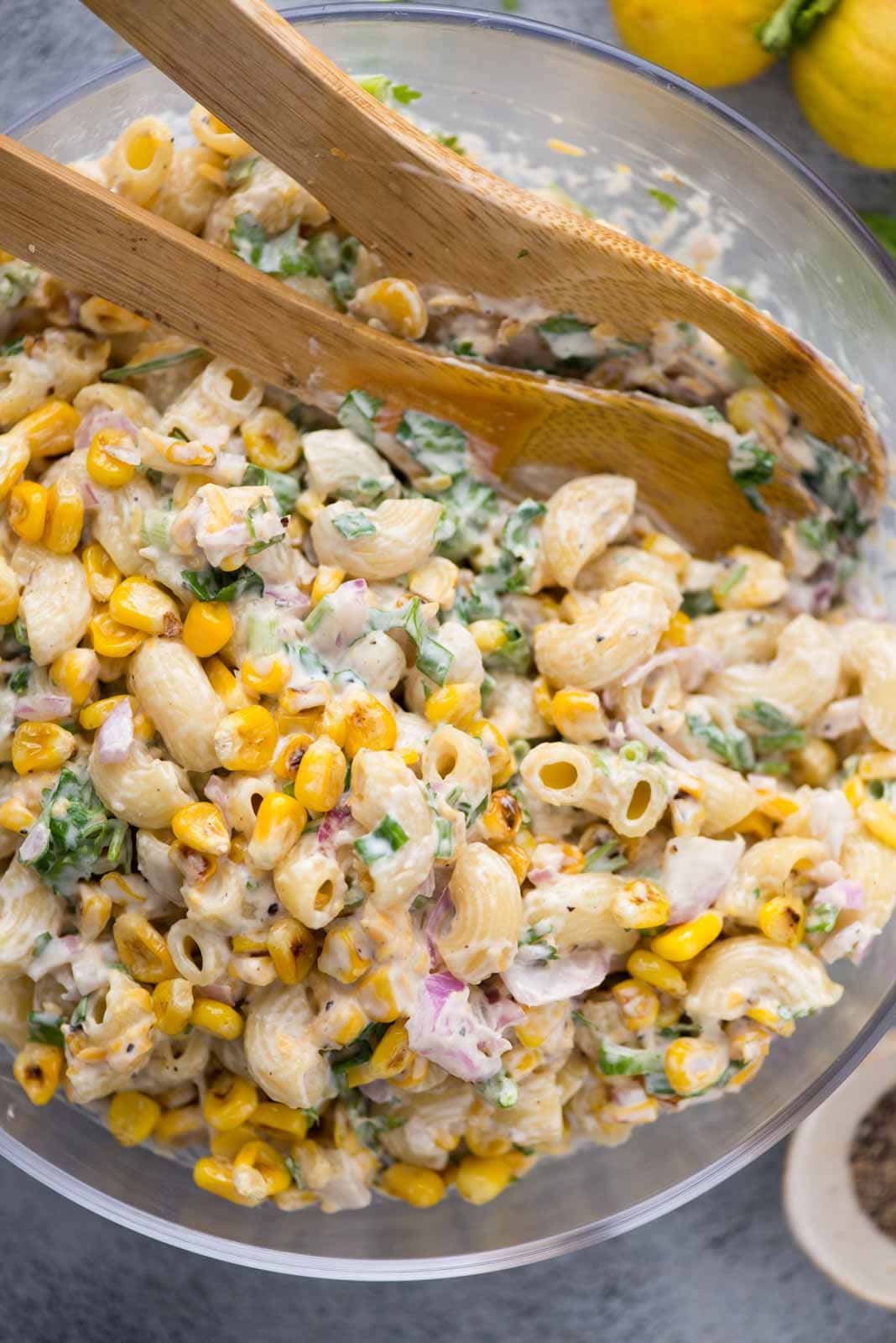 Roasted corn pasta salad tossed in a mayo-based dressing with wooden spatulas.