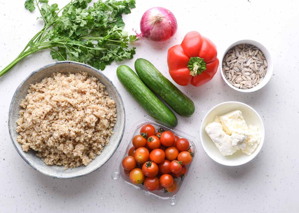 Quinoa Salad Ingredients laid out on the surface - quinoa, cherry tomato, peta cheese and vegetables.