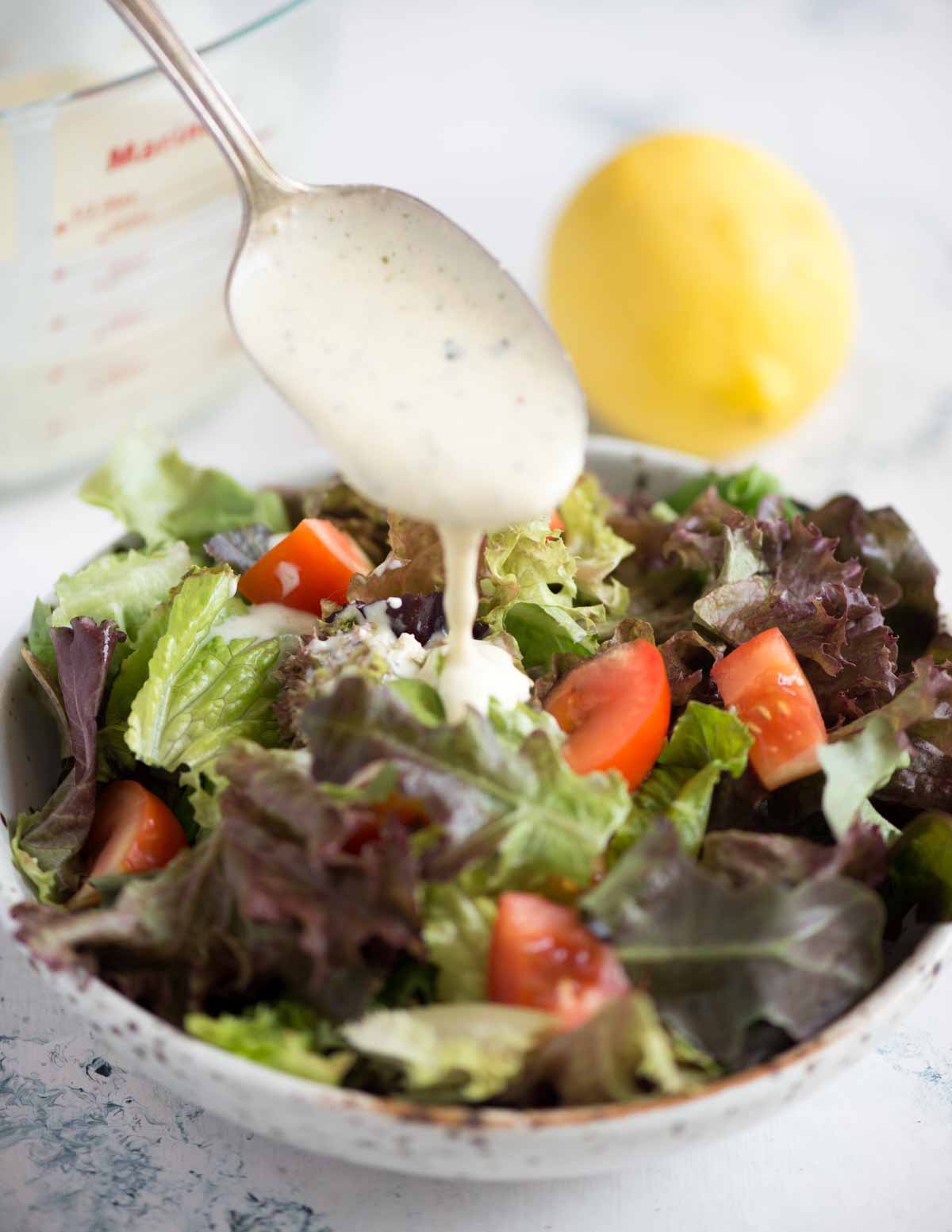 Picture of spoonful of Italian Parmesan Peppercorn dressing added to a leafy vegetable salad in a bowl.