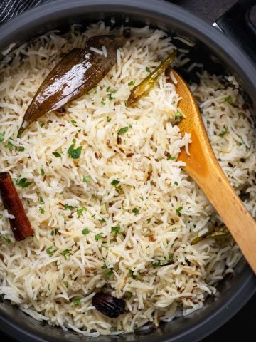 Picture of Jeera rice cooked in a Dutch oven with spices like bay leaf, cumin, cinnamon and chopped coriander leaves sprinkled on top.
