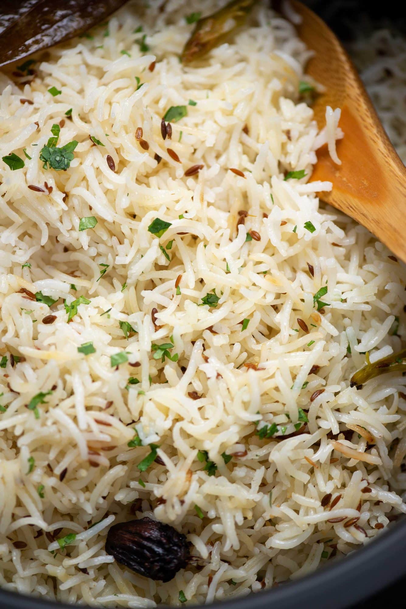 Close up view of jeera rice with a ladle. Jeera rice has cumin, onions, chillies and chopped coriander leaves shown.