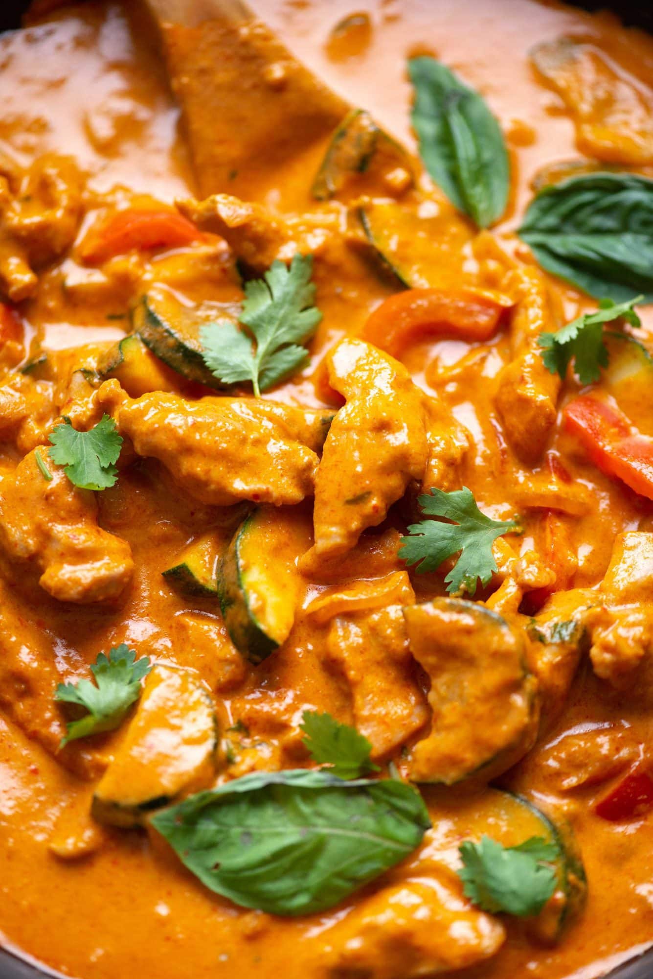 Close up view of Thai red curry with a rich and creamy curry sauce, prepared in a skillet. Has basil and cilantro leaves as garnish.