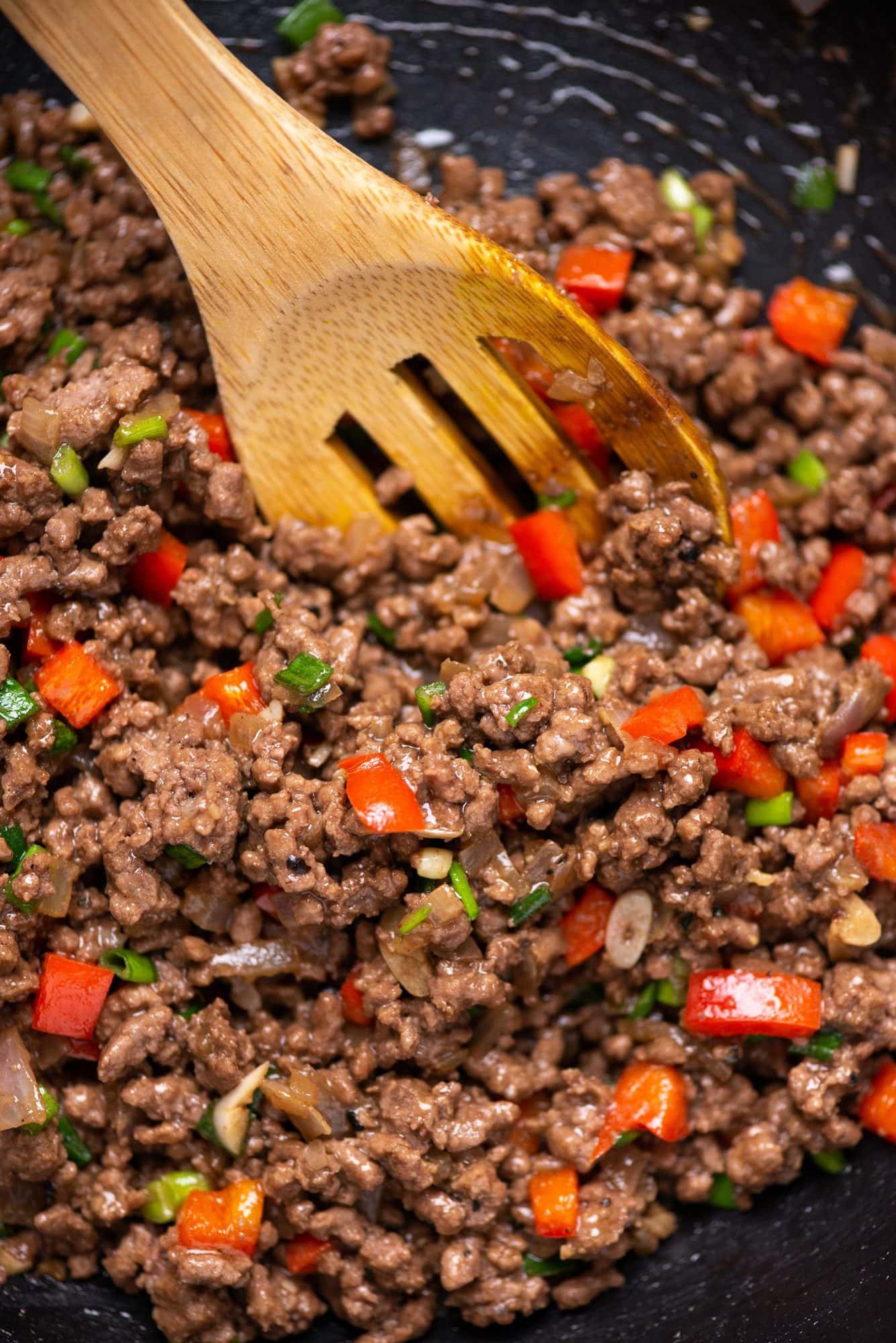 Close up picture of korean inspired juicy ground beef having red bell pepper and green onion stir fried in a wok with a wooden laddle.