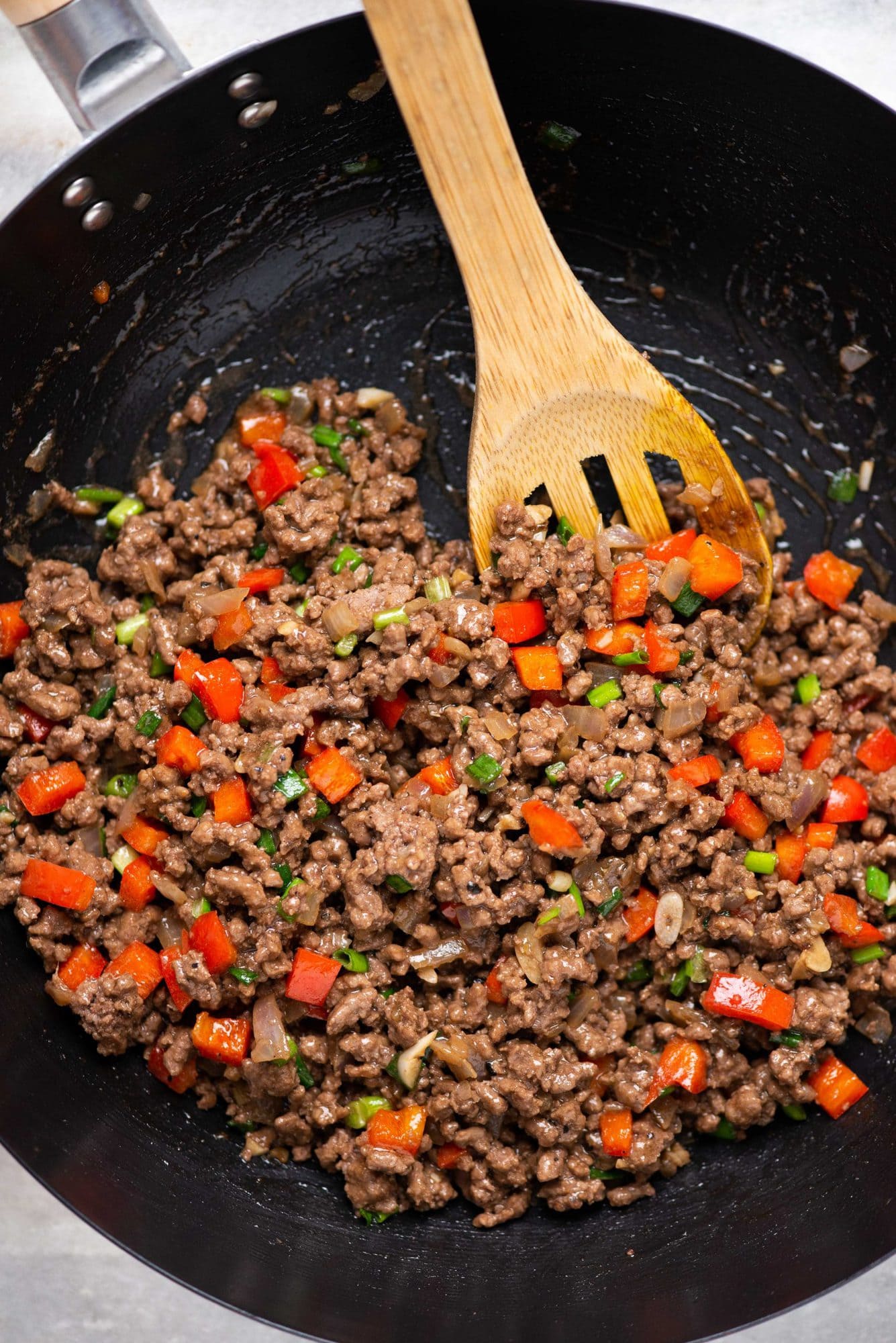 Top view of korean inspired juicy ground beef having red bell pepper and green onion stir fried in a wok with a wooden laddle.