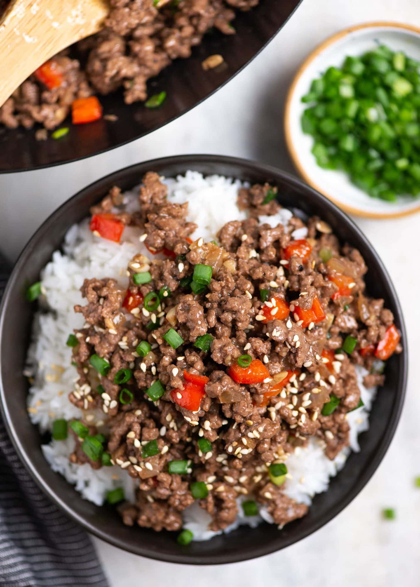 Top view of korean inspired juicy ground beef having red bell pepper and green onion stir fried served in a bowl on top of white rice.