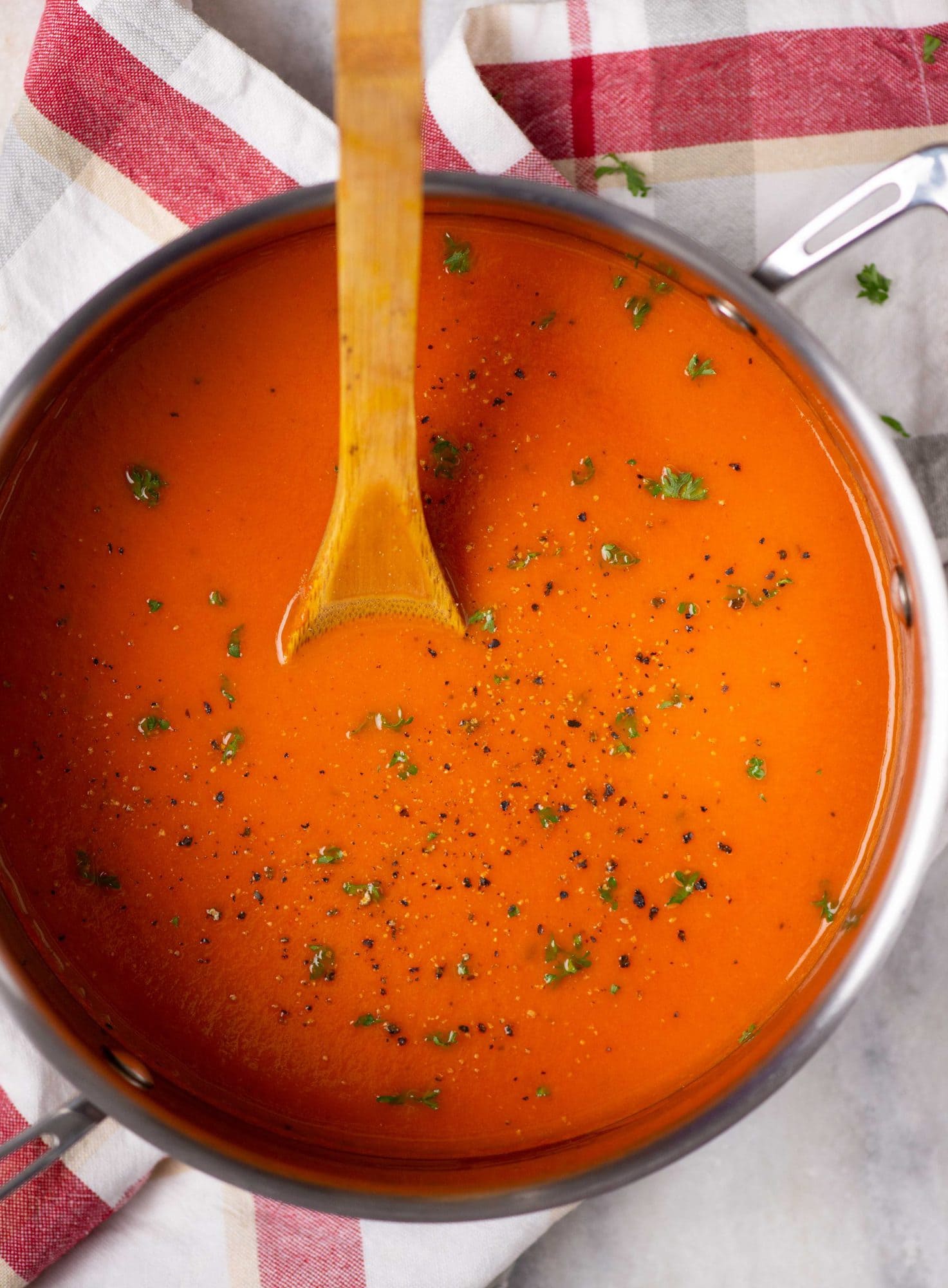 Classic tomato soup is homemade in a soup pot with a chopped basil garnished on top and wooden ladle shown in the image.