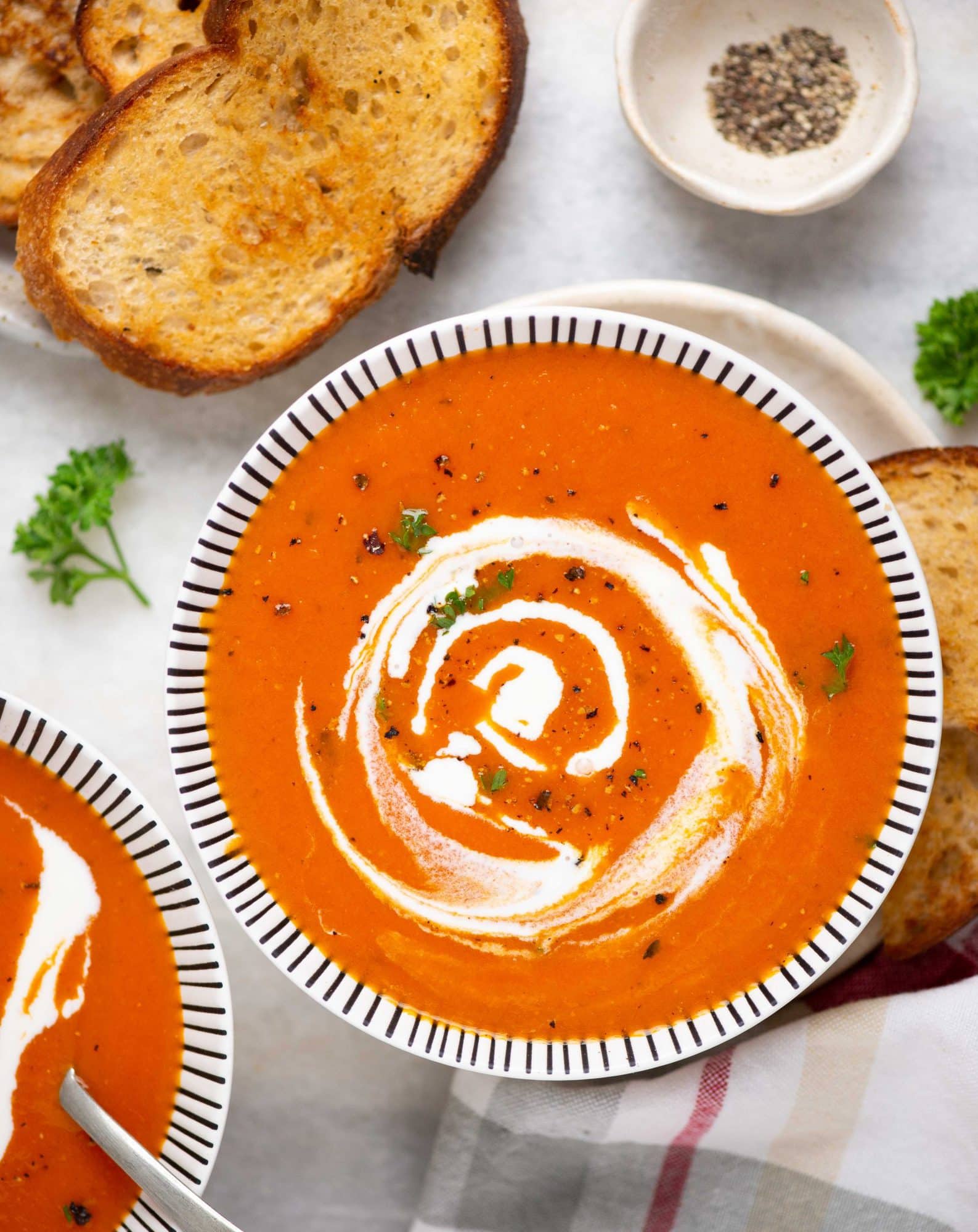 Top view image of tomato soup served in white bowl and cream and basil is garnished on top.