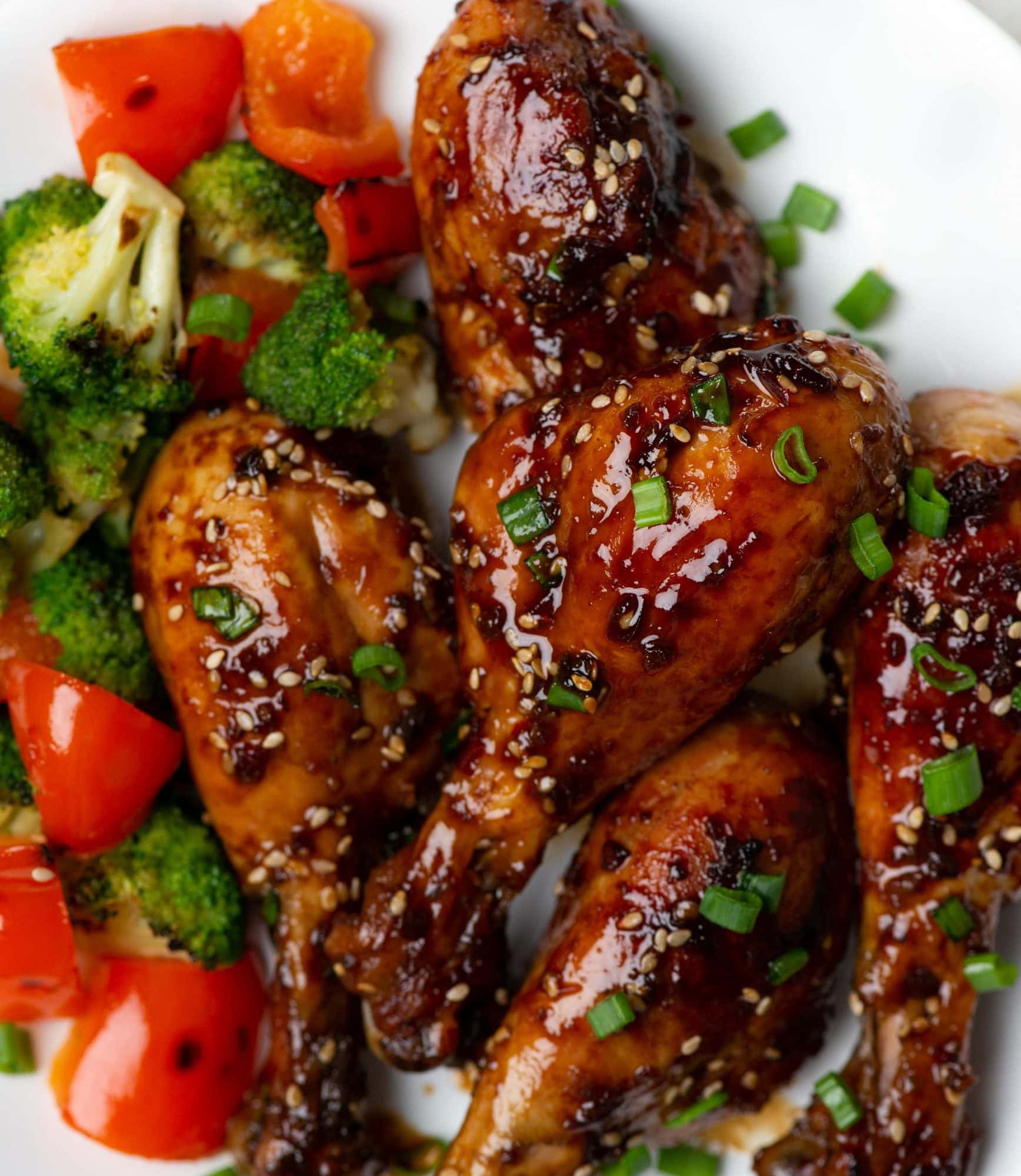 Close up of Honey soy baked chicken drumsticks garnished with green onion slices. Served with roasted broccoli and bell pepper.