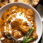 Chicken korma in a white plate with chillies, almonds and cream.