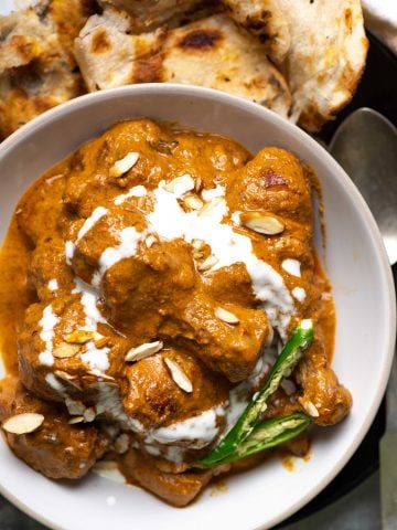 Chicken korma in a white plate with chillies, almonds and cream.