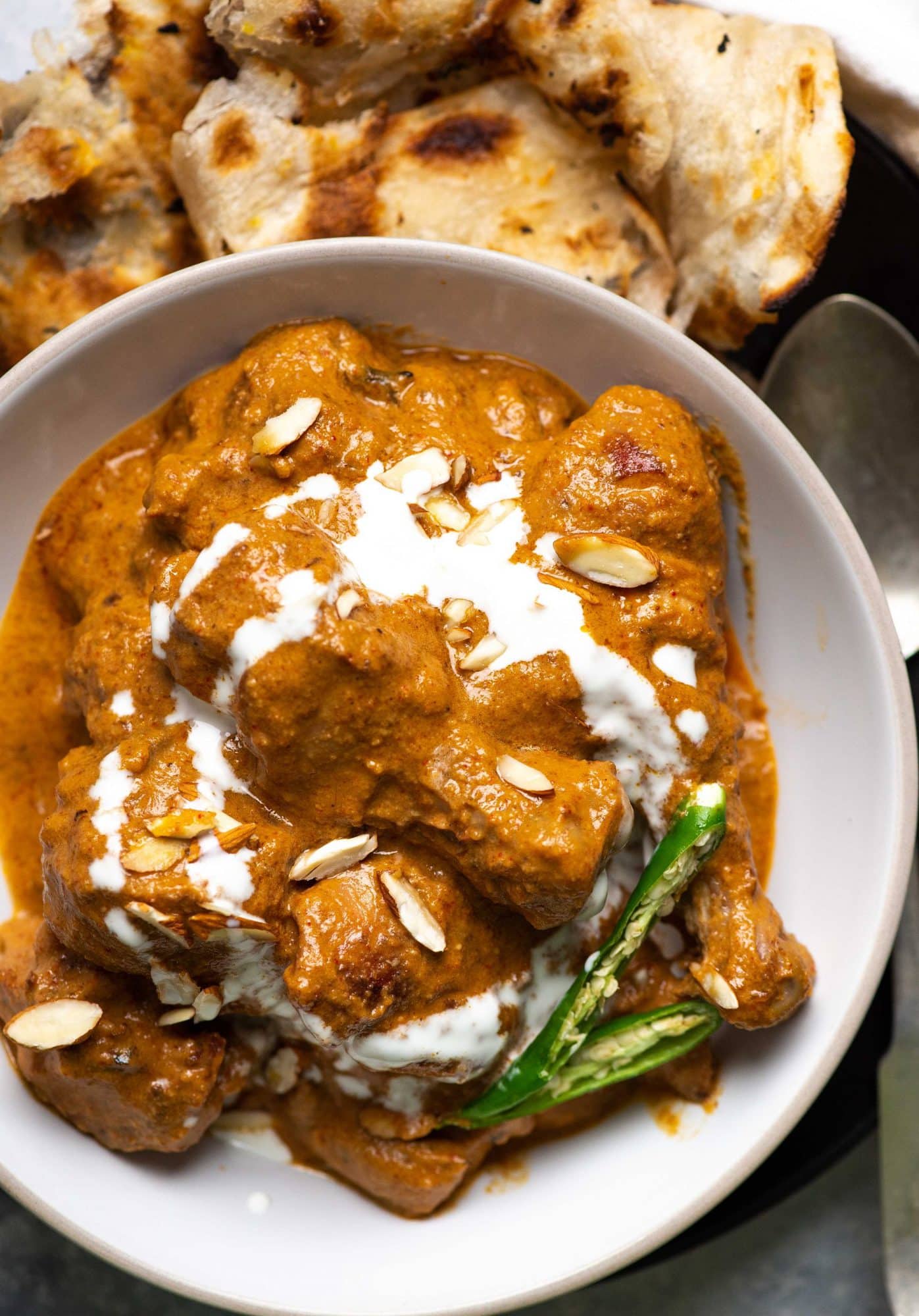 Plated picture of rich chicken korma in a white plate with almonds, chillies and cream on top.