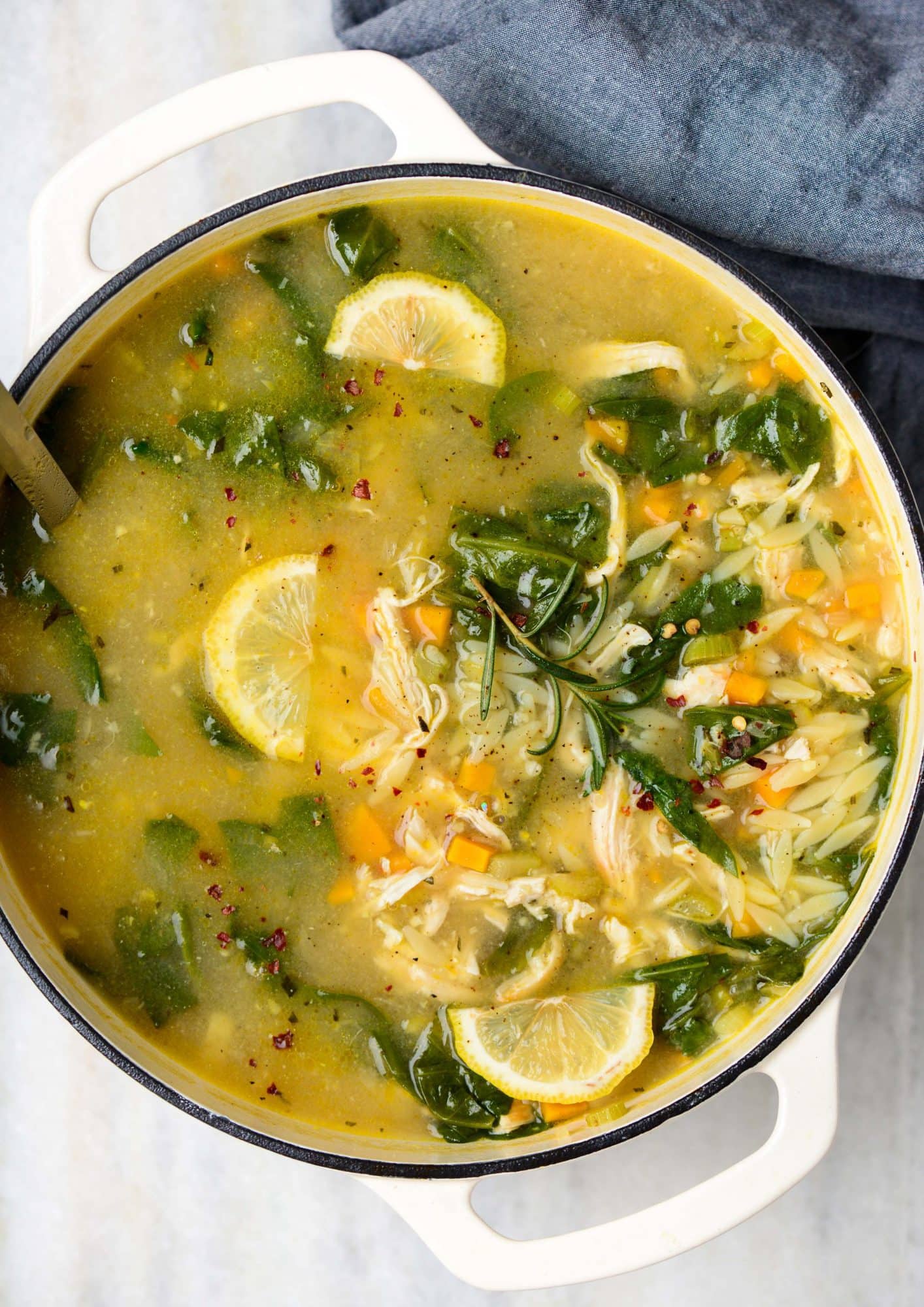 Lemon chicken orzo soup made in a dutch oven with chicken, orzo, baby spinach, celery and lemon wedges.