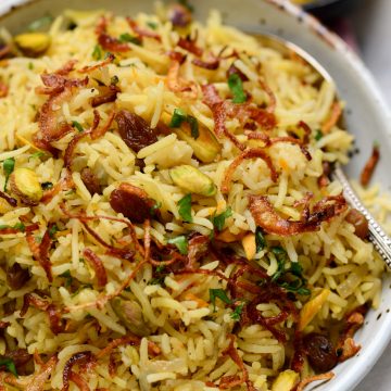 Plated shot of Rice pilaf made with basmati, mild spices, dry fruits, nuts in butter with caramelized onions as garnish