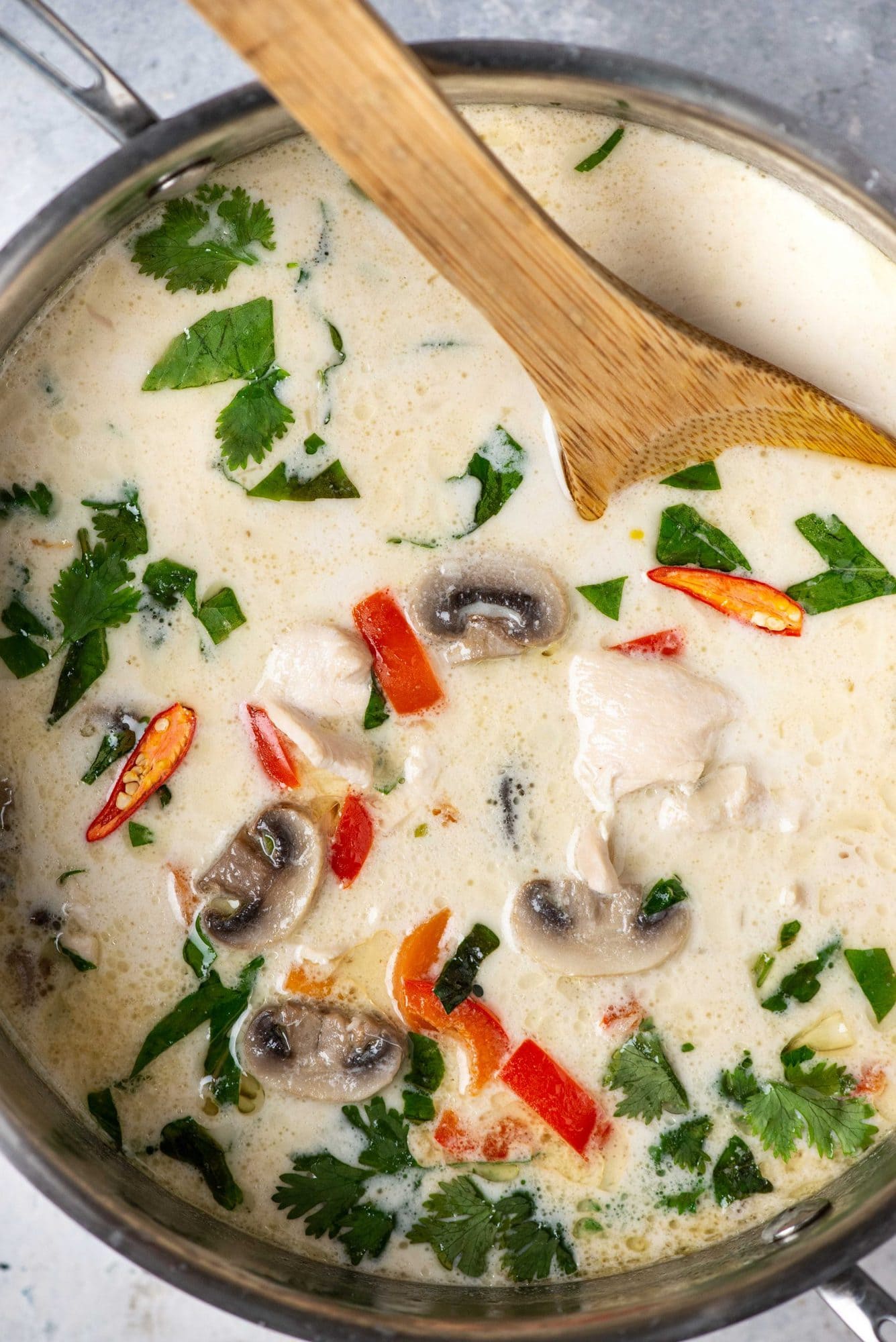 Thai coconut chicken soup (Tom kha gai/kai) being prepared in a large pan and stirred with a laddle.