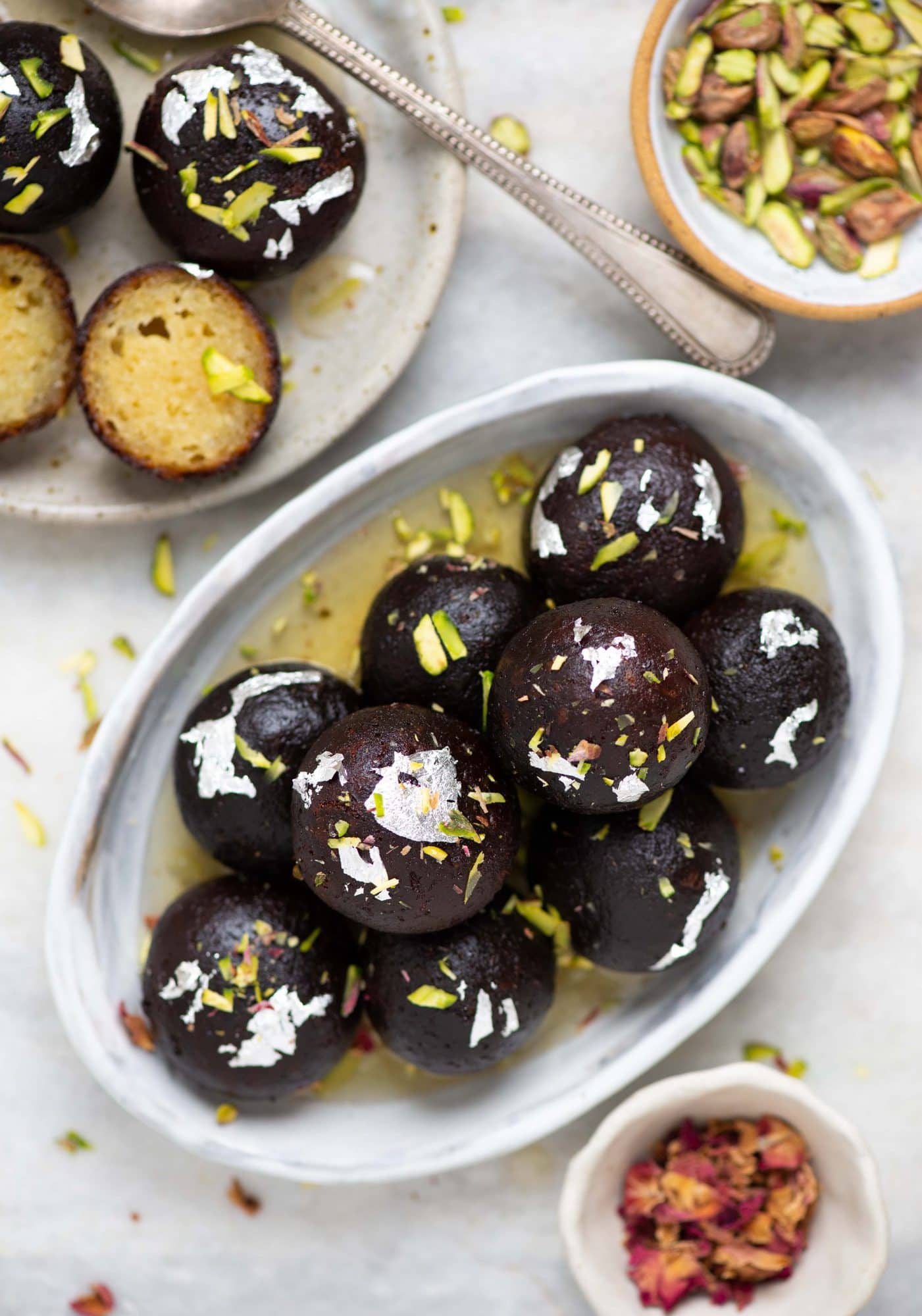 Plate full of kala jamuns. with edible silver foils on them and pista bits as garnish