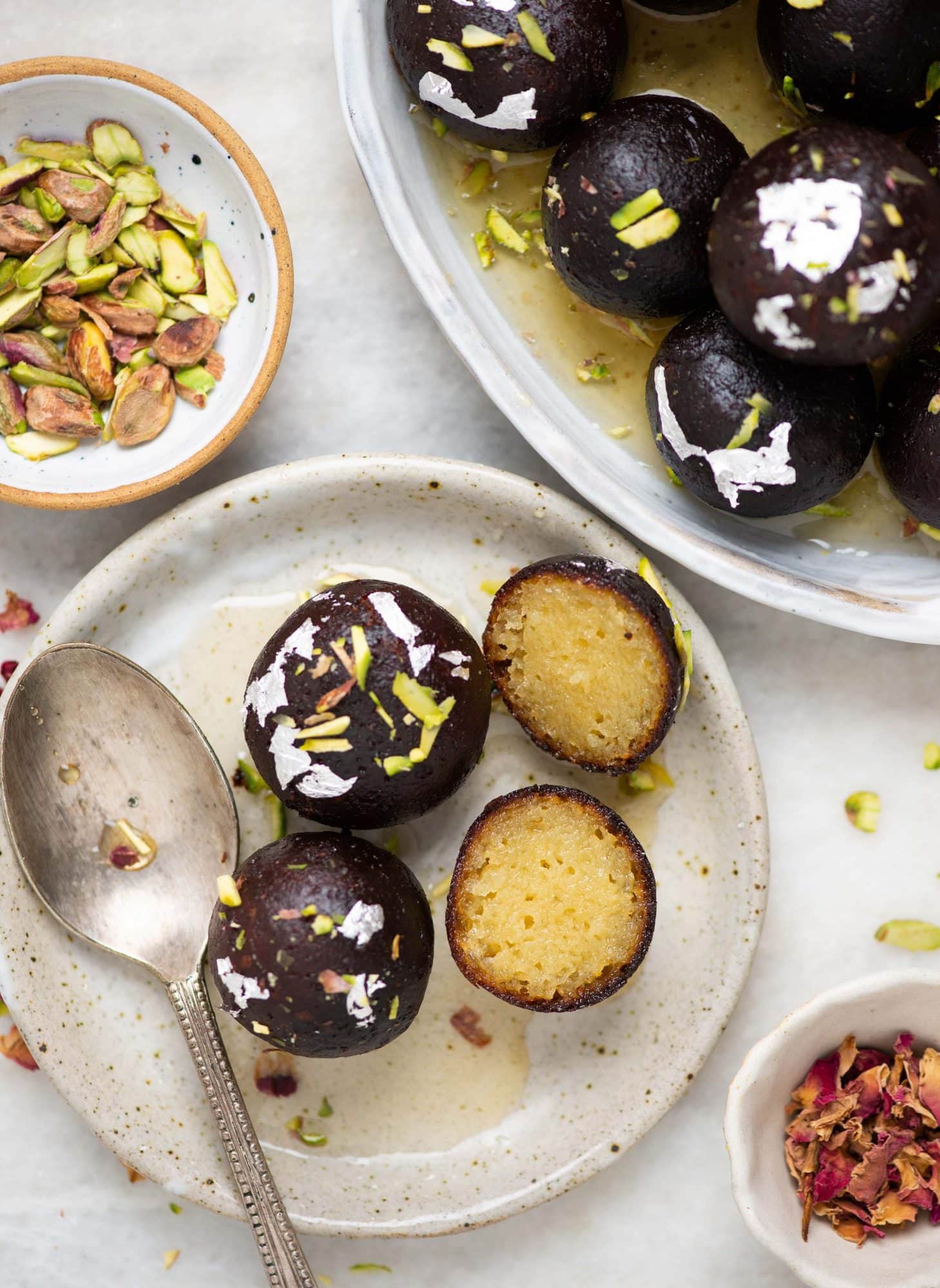 A plate of a couple of kala jamuns and a split halves of a jamun showing its soft juicy core