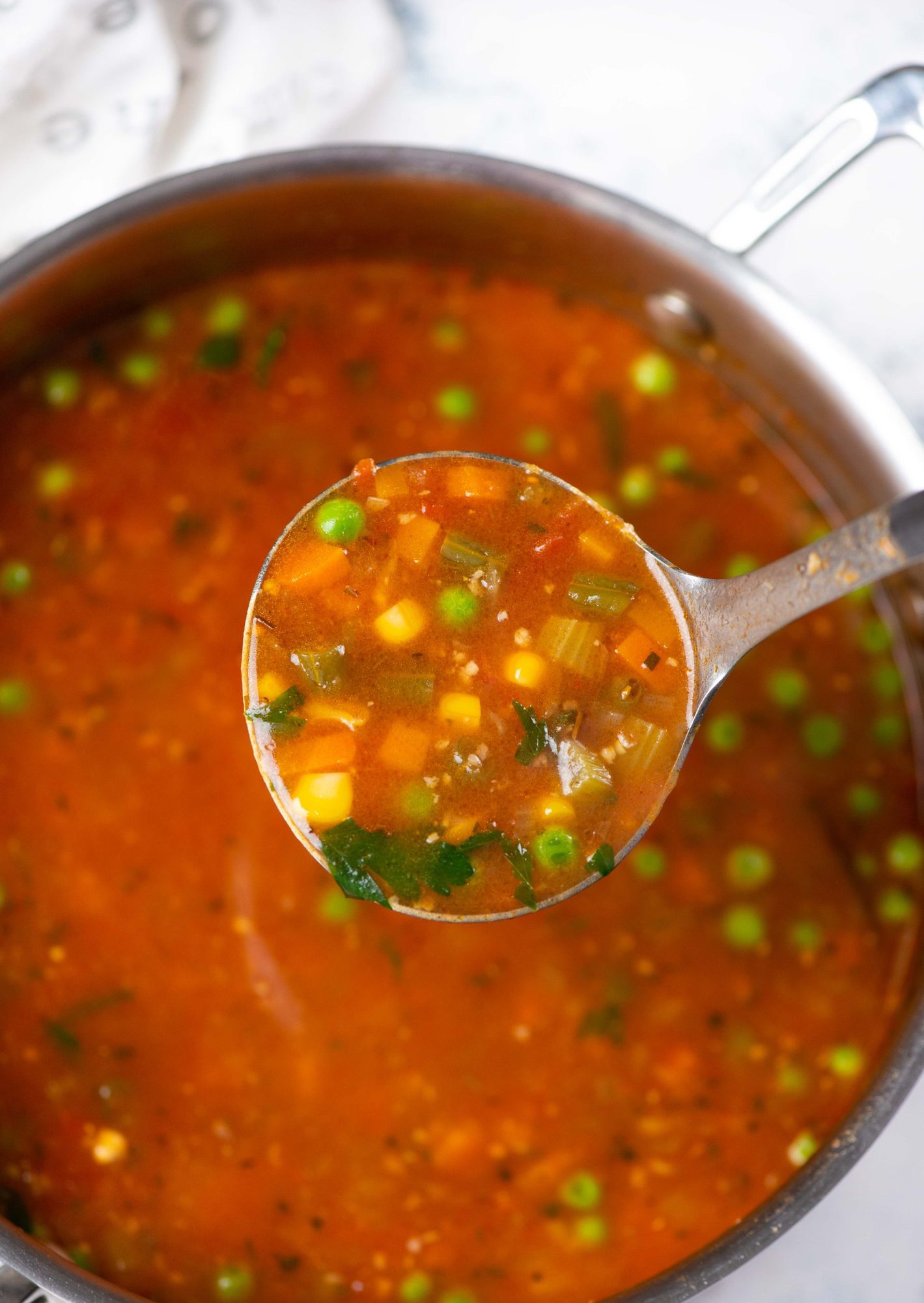 Vegetable soup made of potatoes, carrots, peas and beans shown in a ladle. 