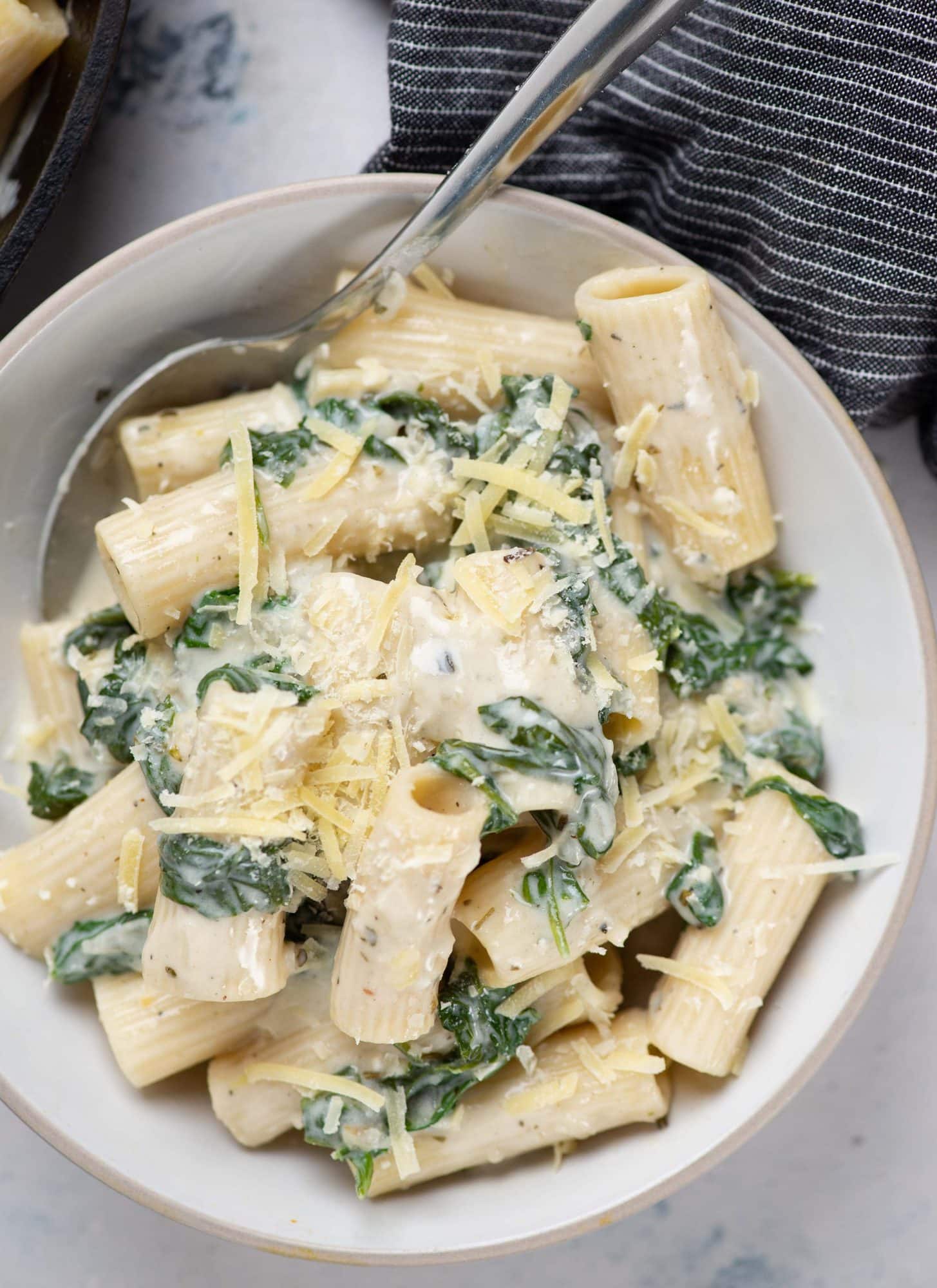 Spinach pasta in a creamy sauce and spinach served in a bowl with shredded cheese garnished on it.