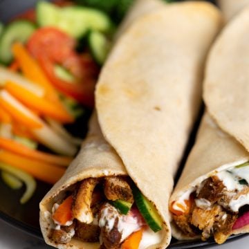 Couple of Chicken Shawarma roll made with juicy grilled chicken, garlic sauce, pickled veggies and served with raw salad on a black plate
