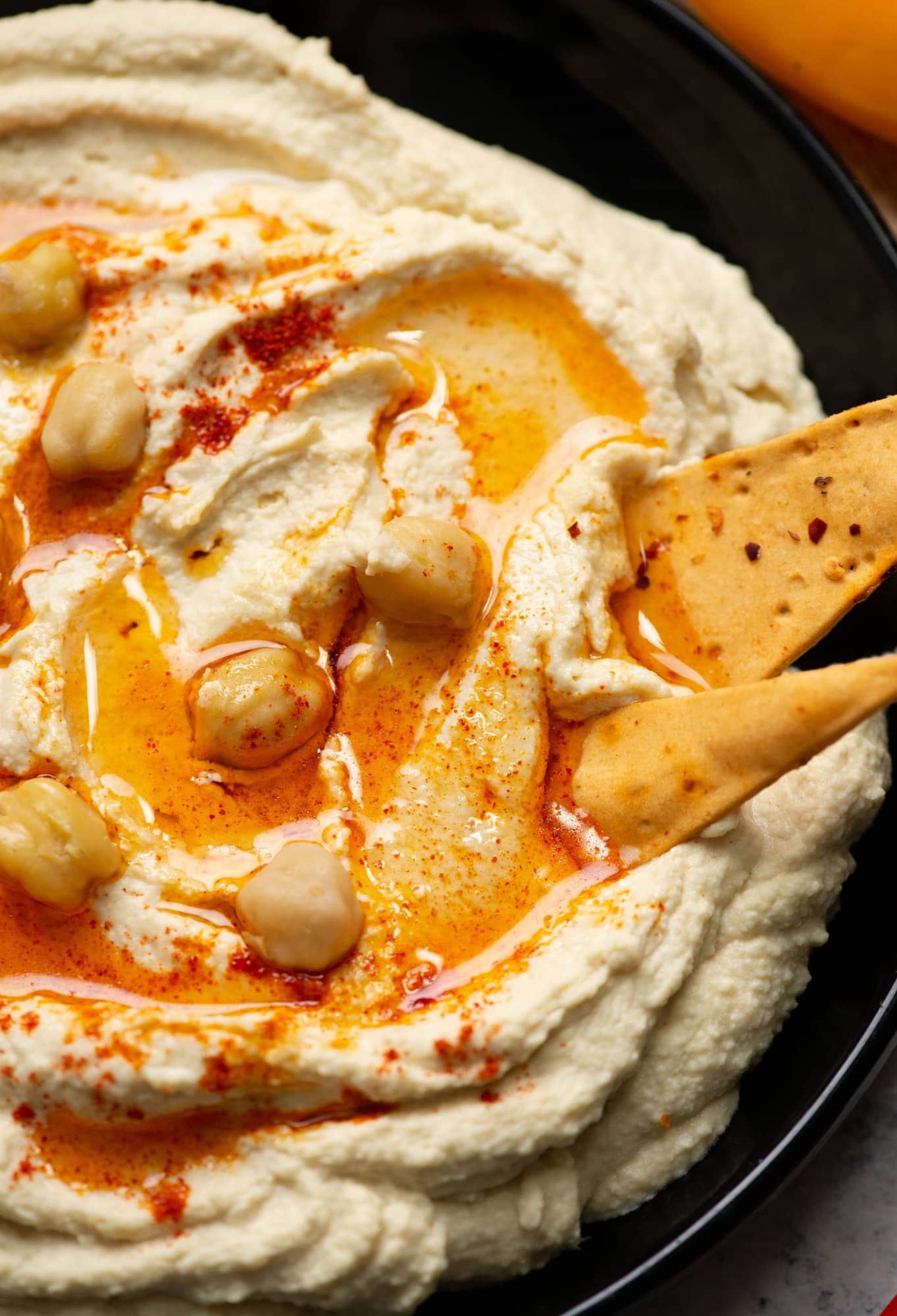 Close view of creamy hummus showing a little olive oil, few whole chickpeas as garnish with pita bites.