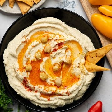 Hummus served on a black plate with garnish and pita bites.