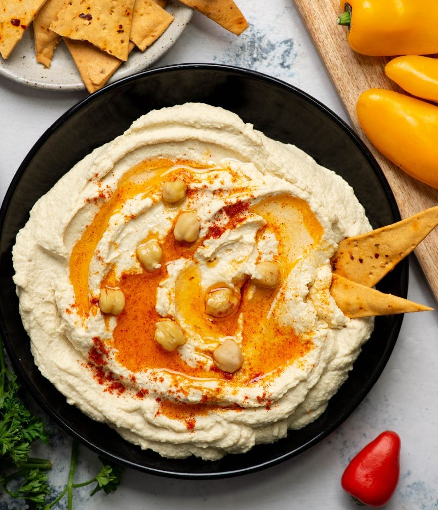 Hummus served on a black plate with garnish and pita bites.