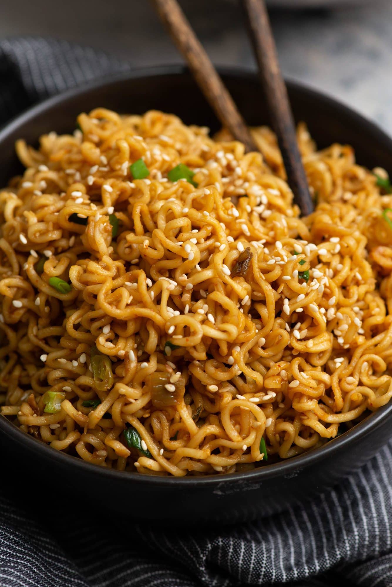 Garlic sesame noodle is served in a black bowl with wooden chopsticks.
