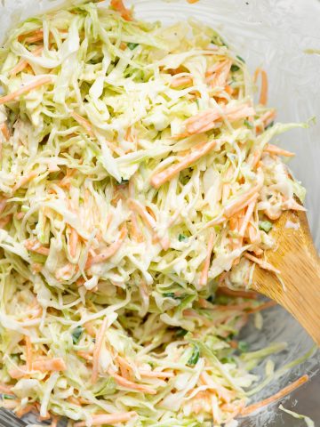 Close up view of creamy cabbage coleslaw with a wooden ladle in it
