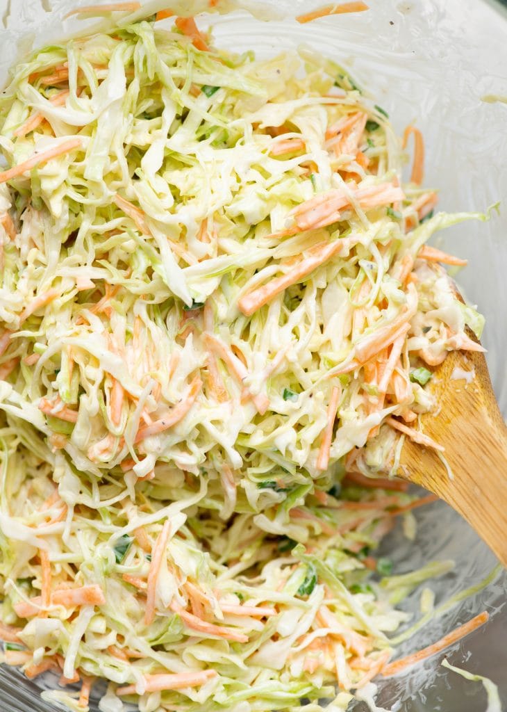 Close up view of creamy cabbage coleslaw with a wooden ladle in it