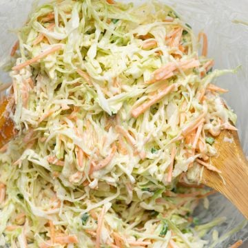 Creamy coleslaw made in a bowl shown with a wooden ladle