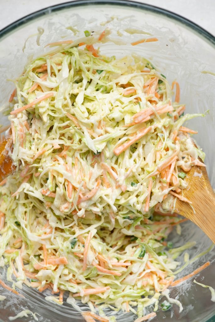 Creamy coleslaw made in a bowl shown with a wooden ladle