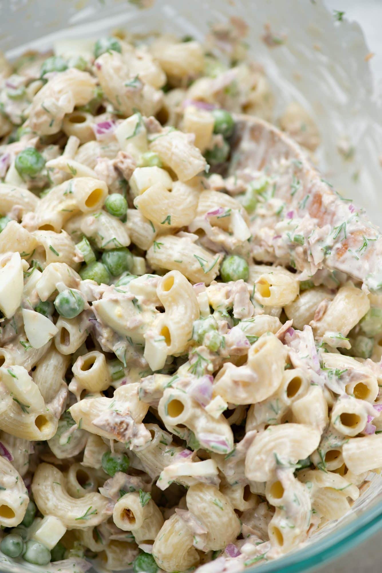 Close up of chunks of tuna, pasta, peas tossed in a creamy mayo-based dressing.