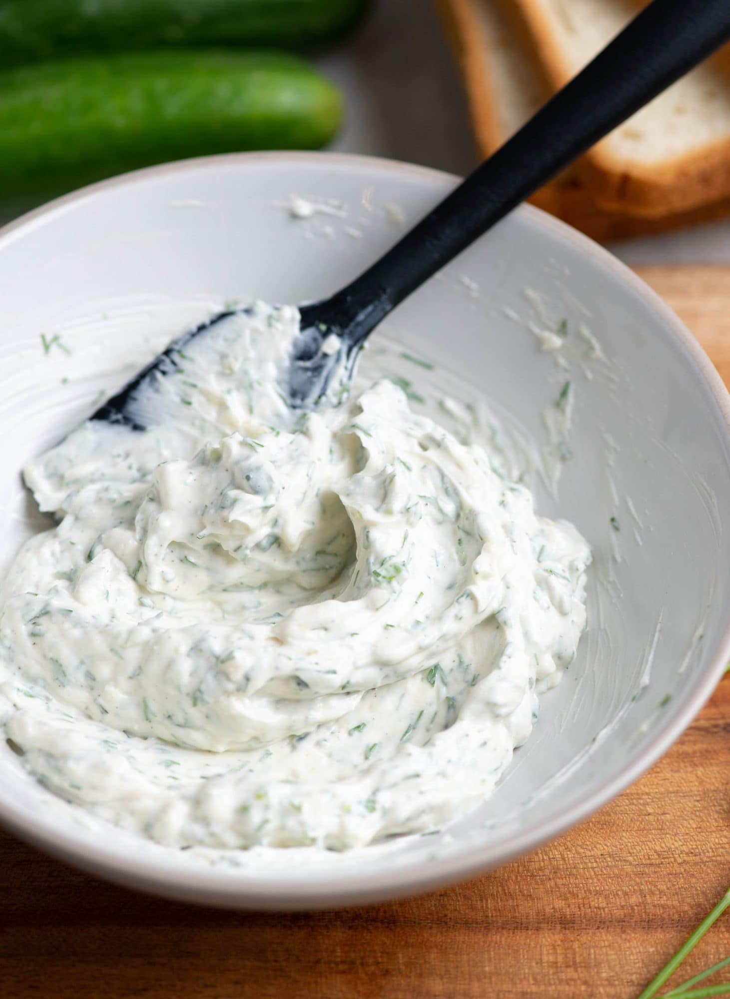 Herby cream cheese spread made in a small bowl and mixes with a black spatula.