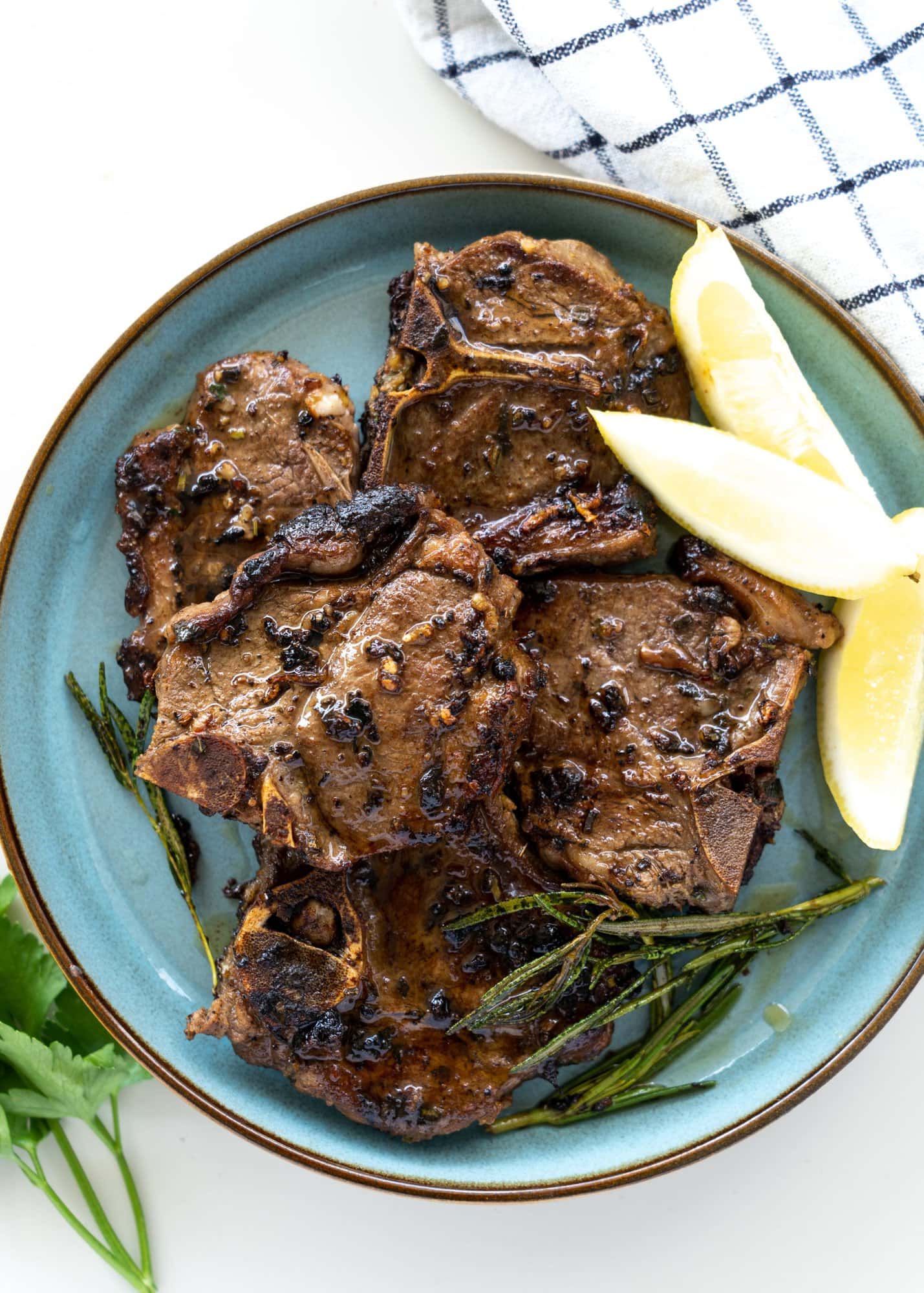 Mediterranean lamb chops seared and served on a blue plate with some lemon slices and parsley.