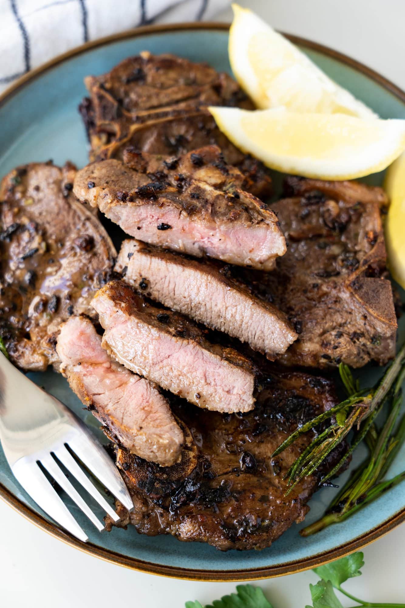 Stack of pan seared lamb chops on a blue plate. One cut to show a pink inside and crusty seared outside.