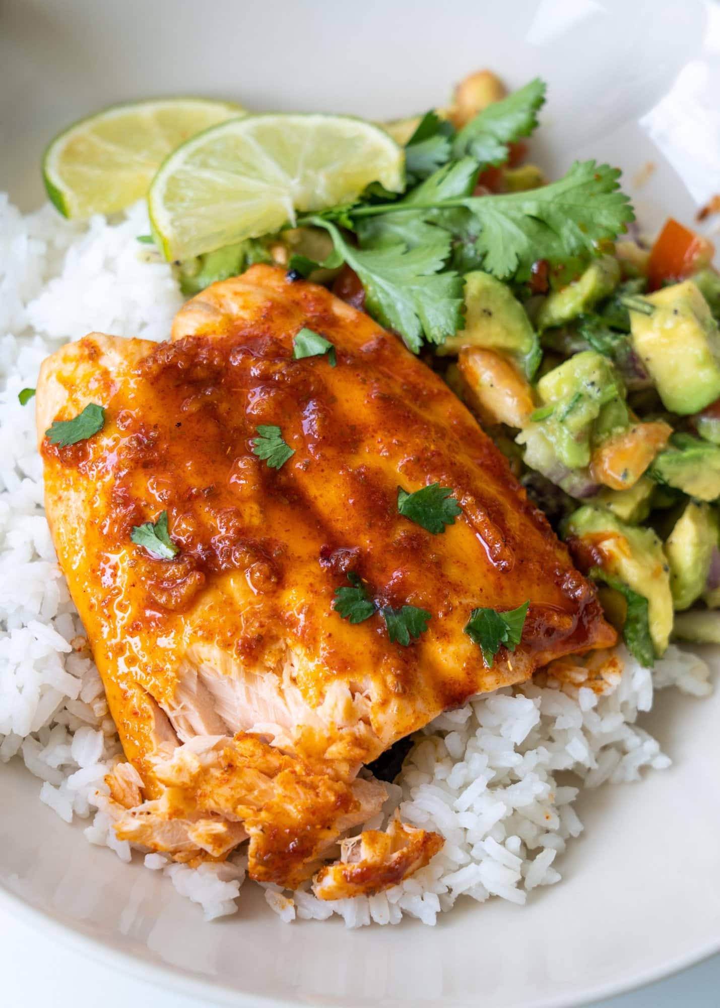 Shown tender and flaky baked salmon  served with rice, avocado salad, lime slice and chopped celery.