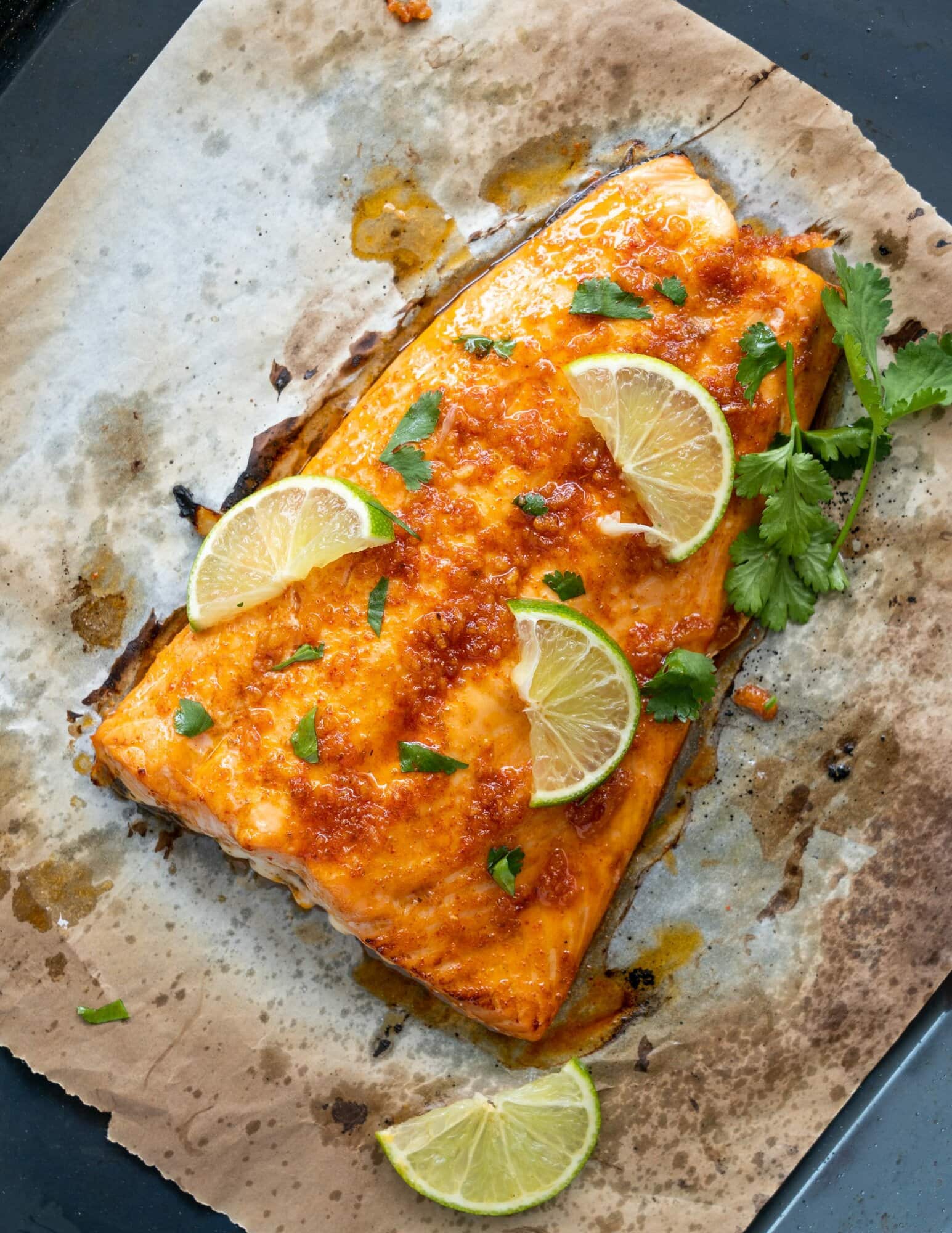 Refreshing and flavorful baked salmon made with a lime and chili marinade shown atop baking sheet with lime slices and chopped celery on top.